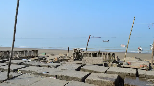 পতেঙ্গা সৈকতের কংক্রিটের ব্লক এবং দূরে বঙ্গোপসাগরের পানিতে ভাসমান জাহাজ ও নৌকা।
