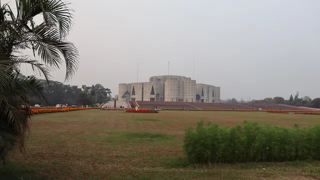 সবুজ লন ও ফুলের বাগানের ওপাশে ঢাকার জাতীয় সংসদ ভবনের দূরবর্তী দৃশ্য।